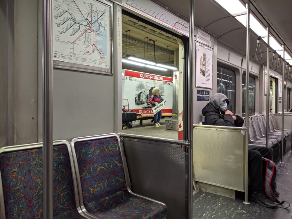 bear playing a keytar next to the quincy center T sign, taken from inside a train