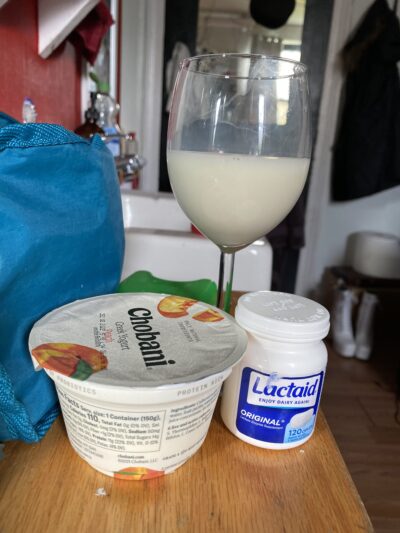 a wine glass full of almond milk, a peach chobani yogurt, a bottle of lactaid