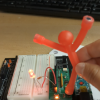 stick figure shaped fridge magnet held above an electronic circuit, where one LED is lit